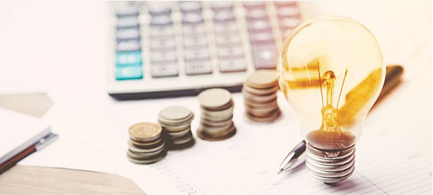 Bombillo encendido junto a monedas y calculadora, representando ideas financieras o ahorro energético.