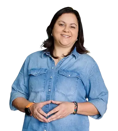 Mujer de pie con camisa de mezclilla azul, sonriendo y con las manos juntas al frente.