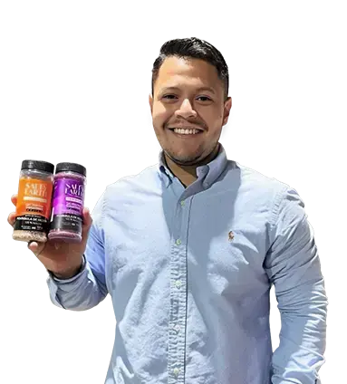 Hombre de pie con camisa celeste sonriendo y sosteniendo dos frascos de condimentos.