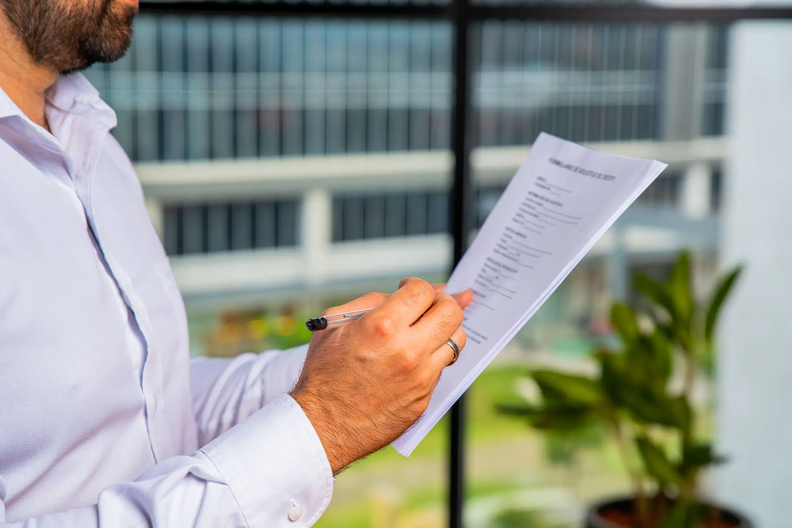 Persona de camisa blanca revisando un documento y tomando notas con un bolígrafo.