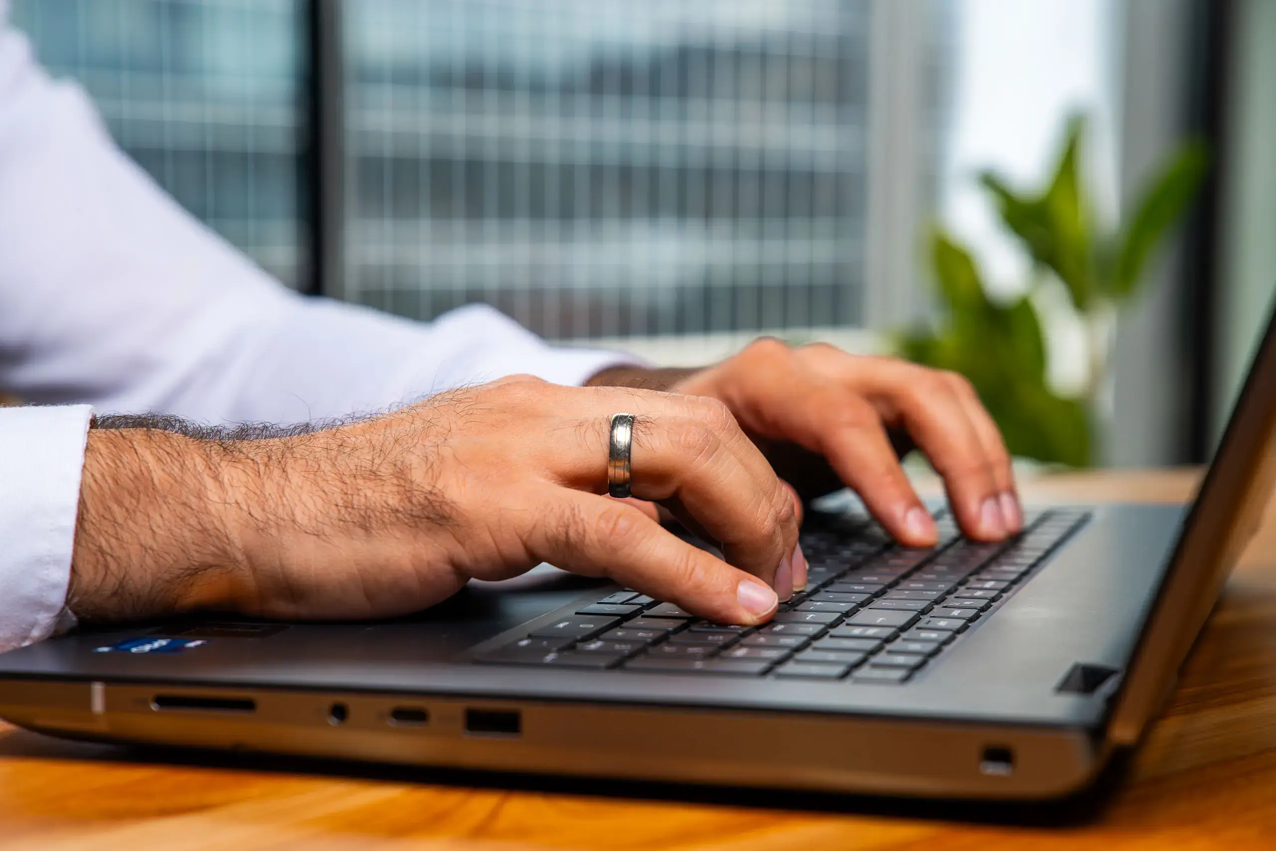 Manos de un hombre escribiendo en el teclado de una computadora portátil sobre una mesa de madera.