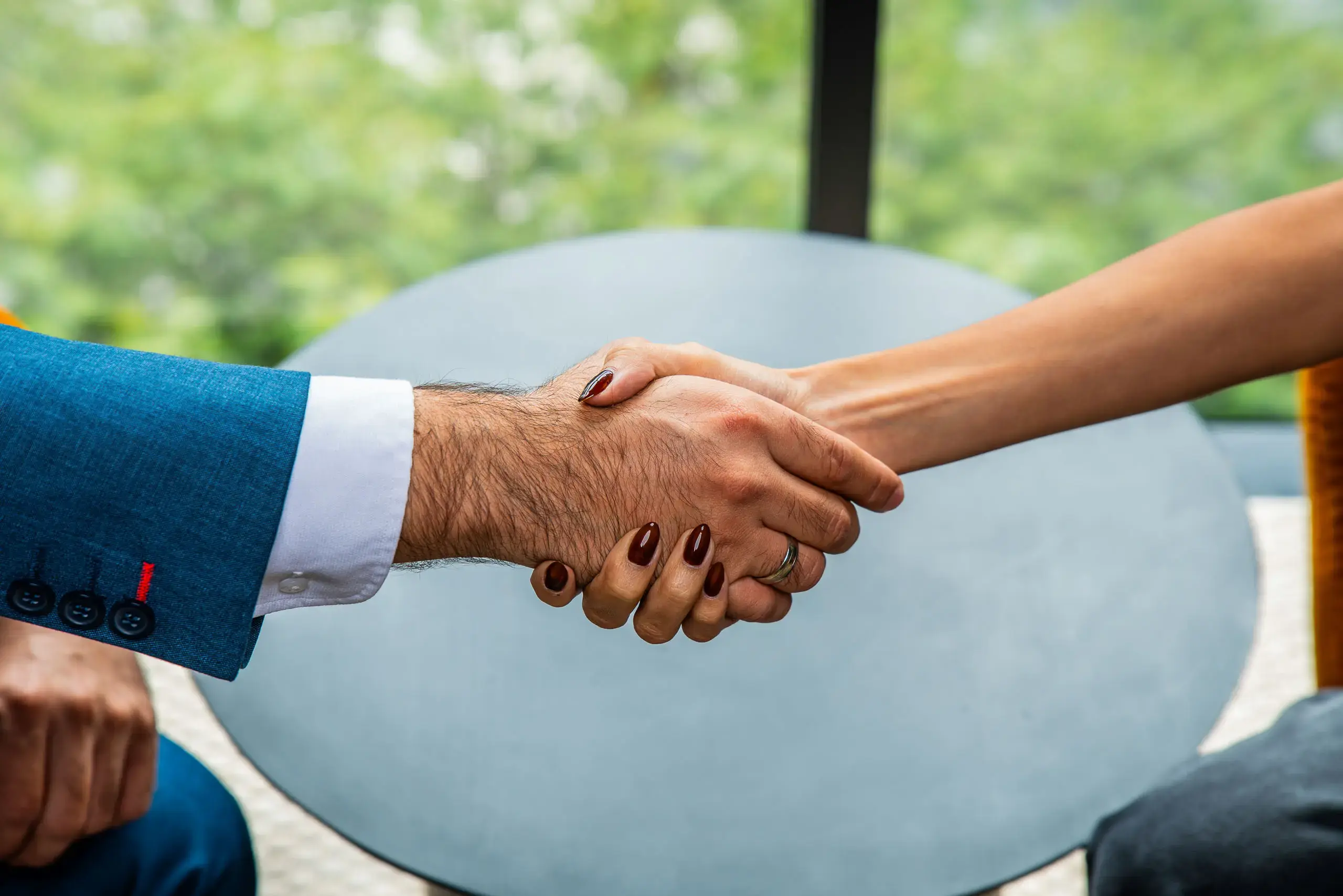 Apretón de manos entre dos personas, una con saco azul y otra con uñas esmaltadas.
