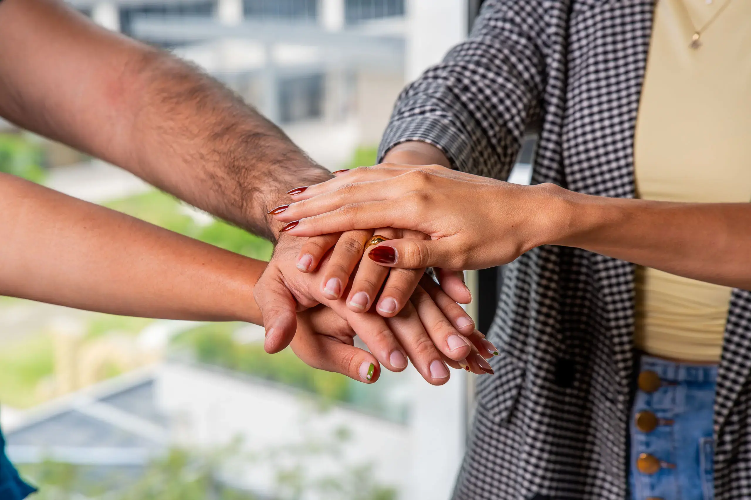 Manos de varias personas unidas en el centro en gesto de trabajo en equipo.