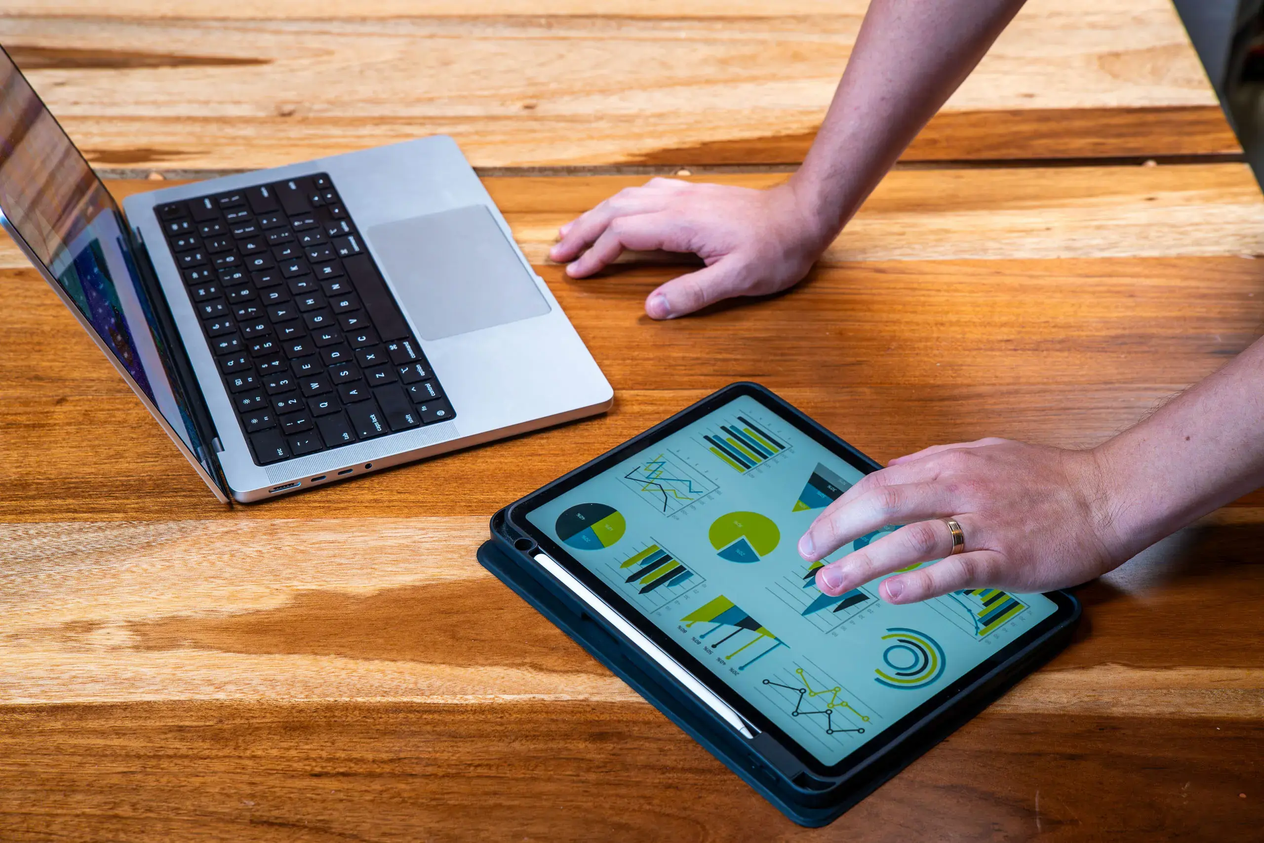 Manos de una persona trabajando con gráficos en una tablet junto a una laptop sobre mesa de madera.