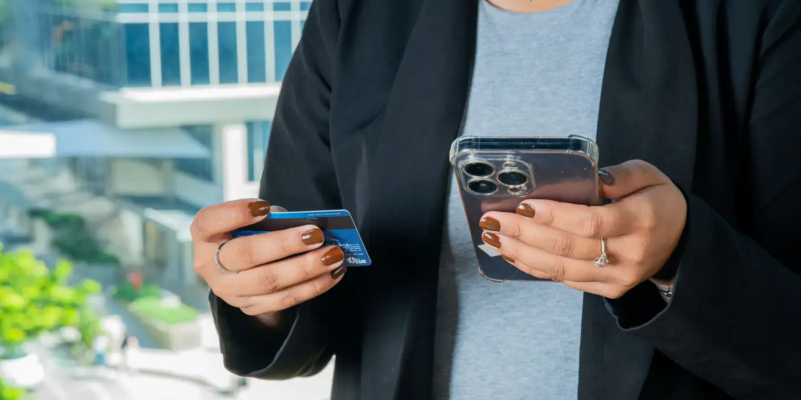 Persona sosteniendo una tarjeta y un teléfono móvil mientras realiza una gestión digital.