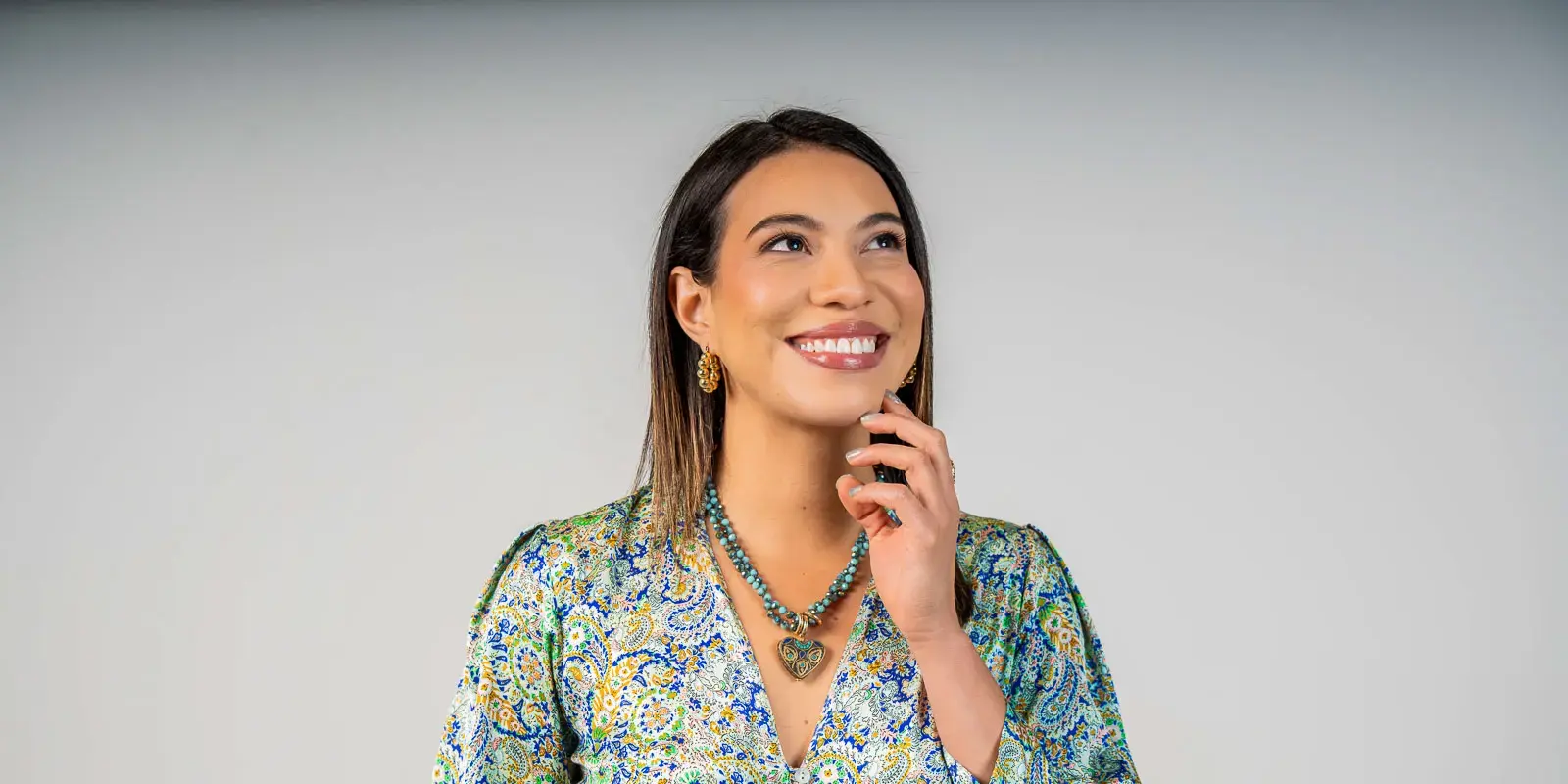 Mujer sonriendo y mirando hacia arriba con la mano en el mentón.