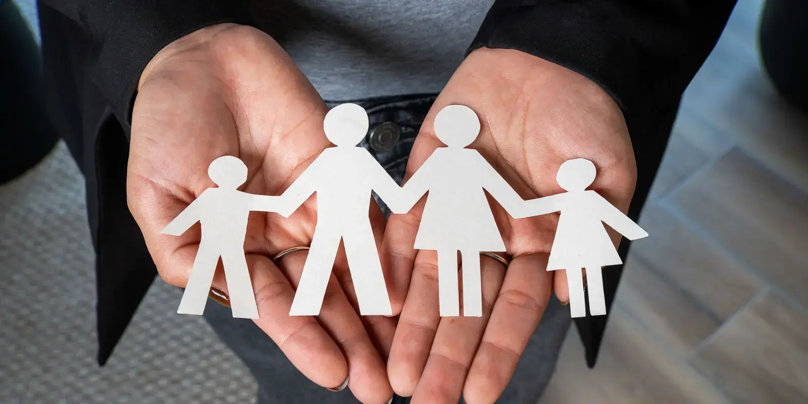 Manos sosteniendo recorte de papel con figuras que representan a una familia.