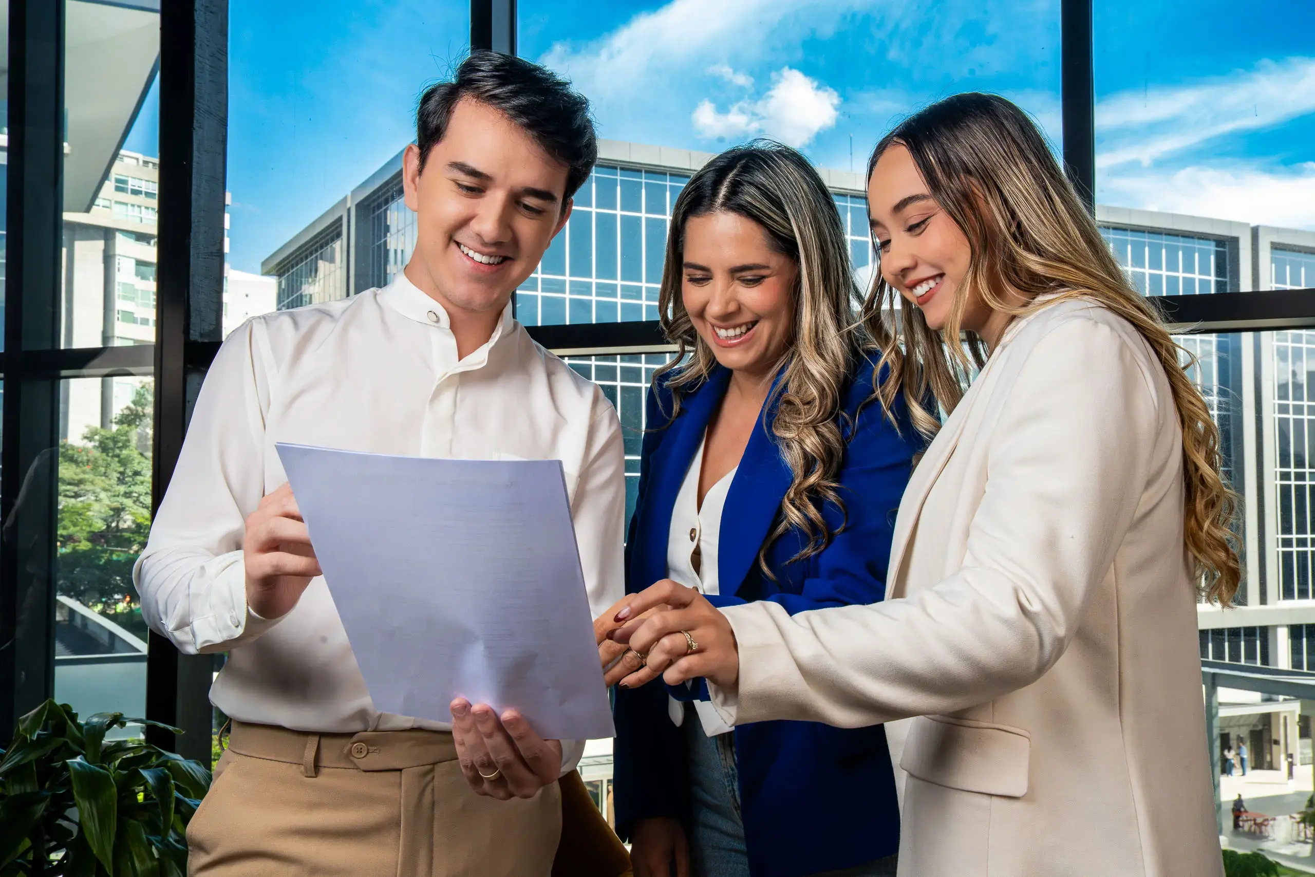 Tres personas revisando juntas un documento en una oficina con ventanales.