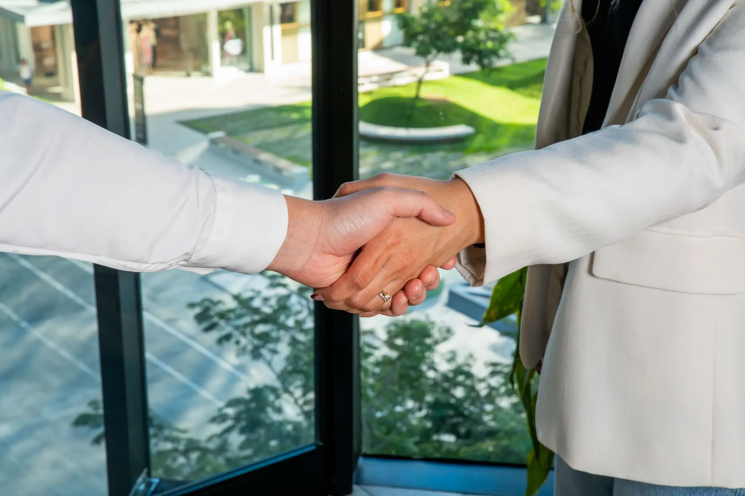 Dos personas estrechando manos en un entorno de oficina con ventanales.