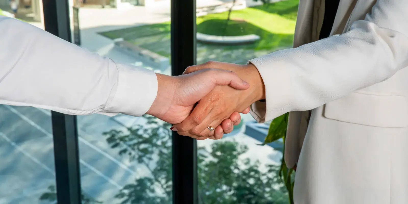 Dos personas estrechando manos en un entorno de oficina con ventanales.