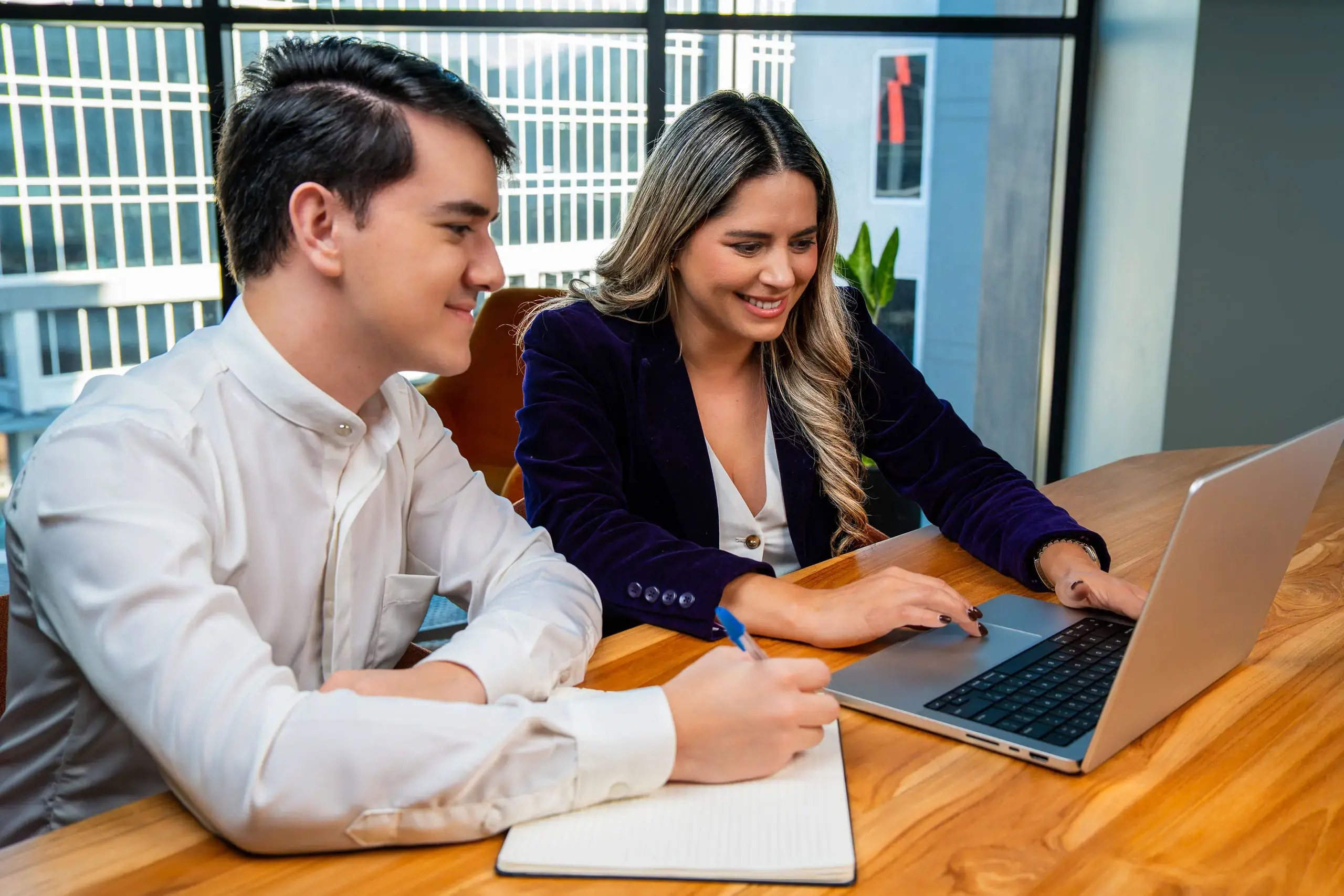 Dos personas trabajando juntas frente a una computadora portátil en una mesa de oficina.