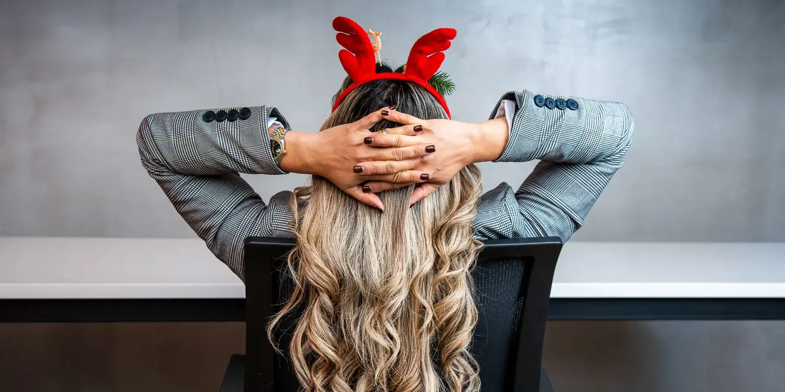 Persona sentada de espaldas en una silla de oficina, con manos entrelazadas detrás de la cabeza y diadema roja con cuernos festivos.