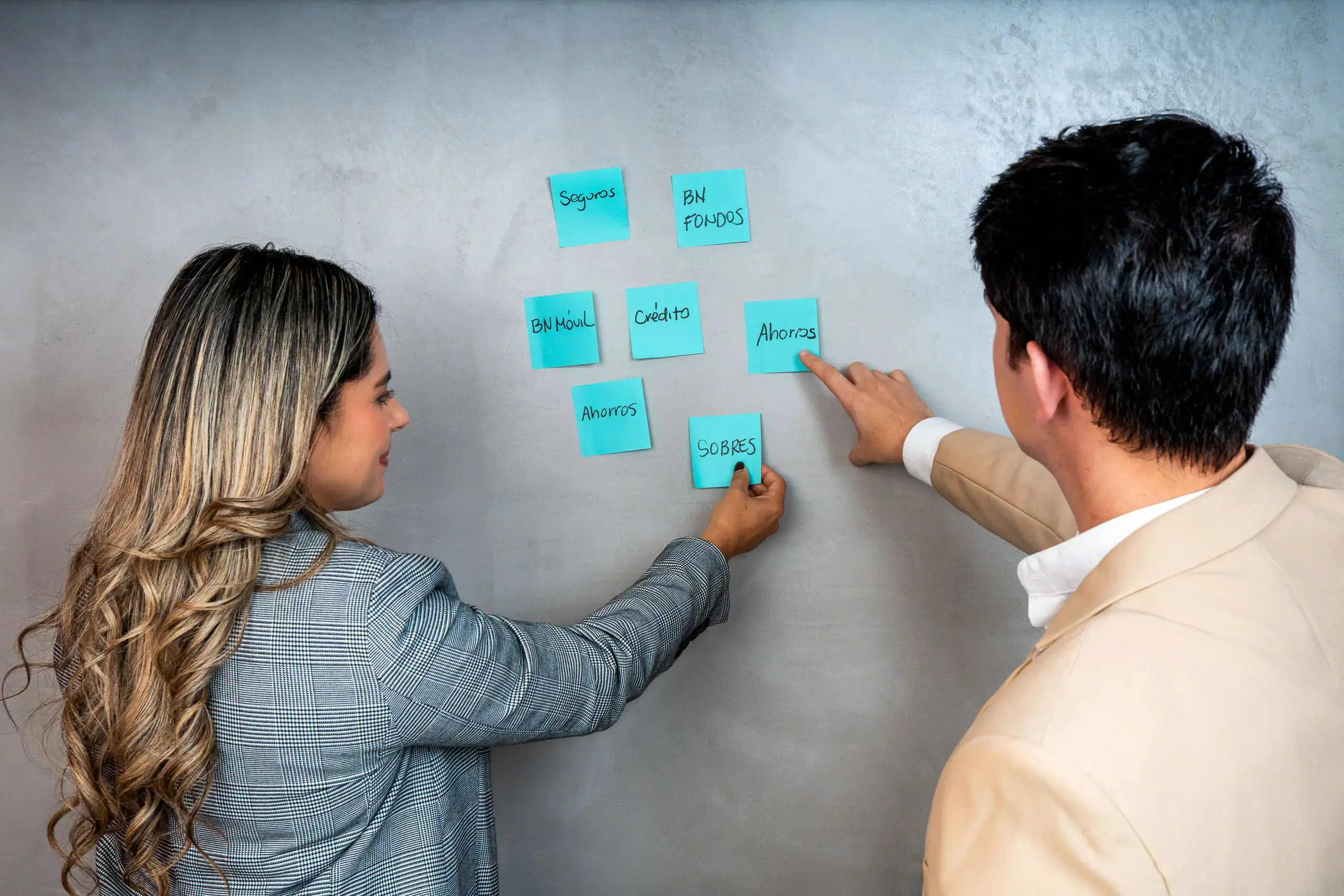 Dos personas organizando notas adhesivas en una pared con diferentes temas escritos.
