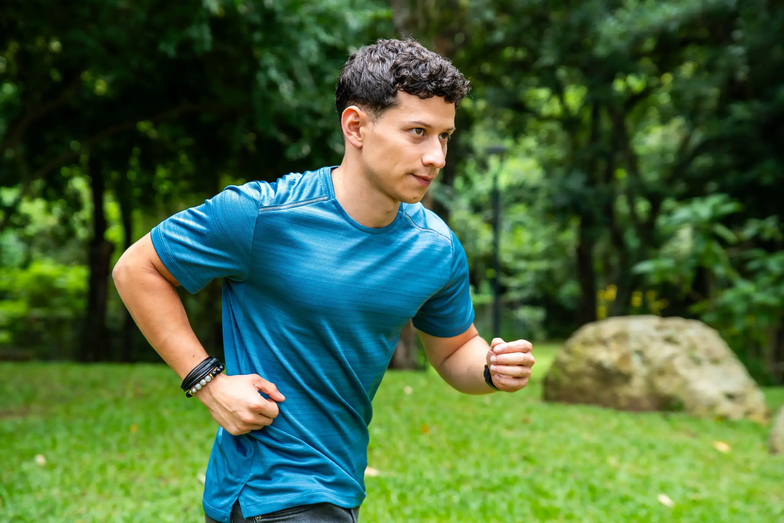 Hombre joven corriendo en un parque con vegetación al fondo.