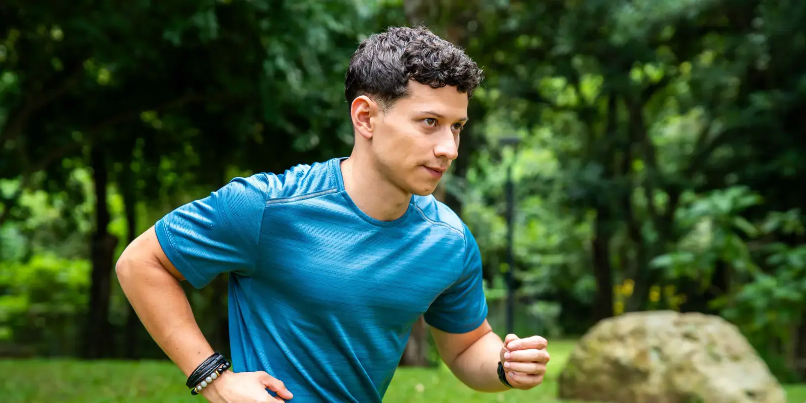 Hombre joven corriendo al aire libre en un parque rodeado de vegetación.