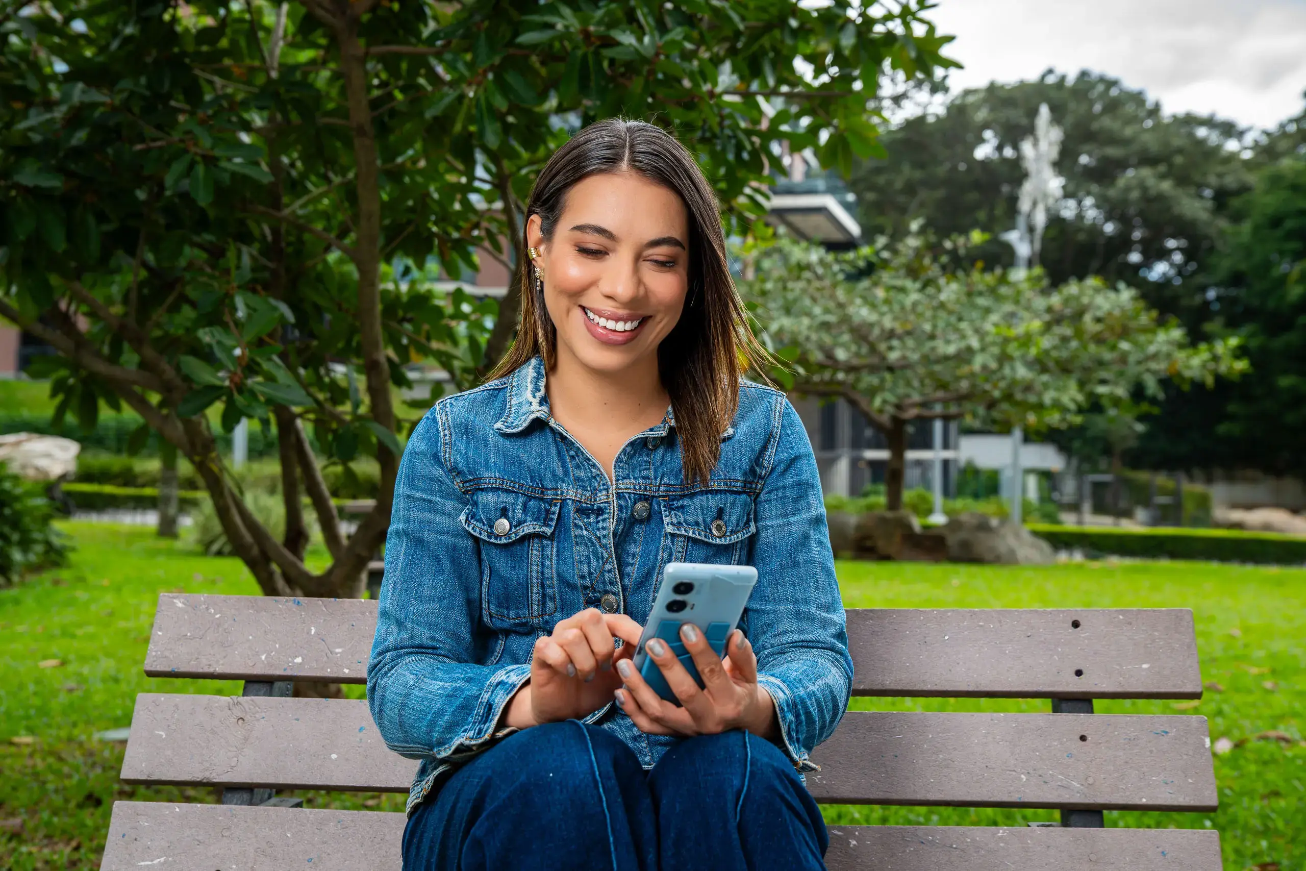 Mujer sentada en una banca al aire libre usando su teléfono móvil.
