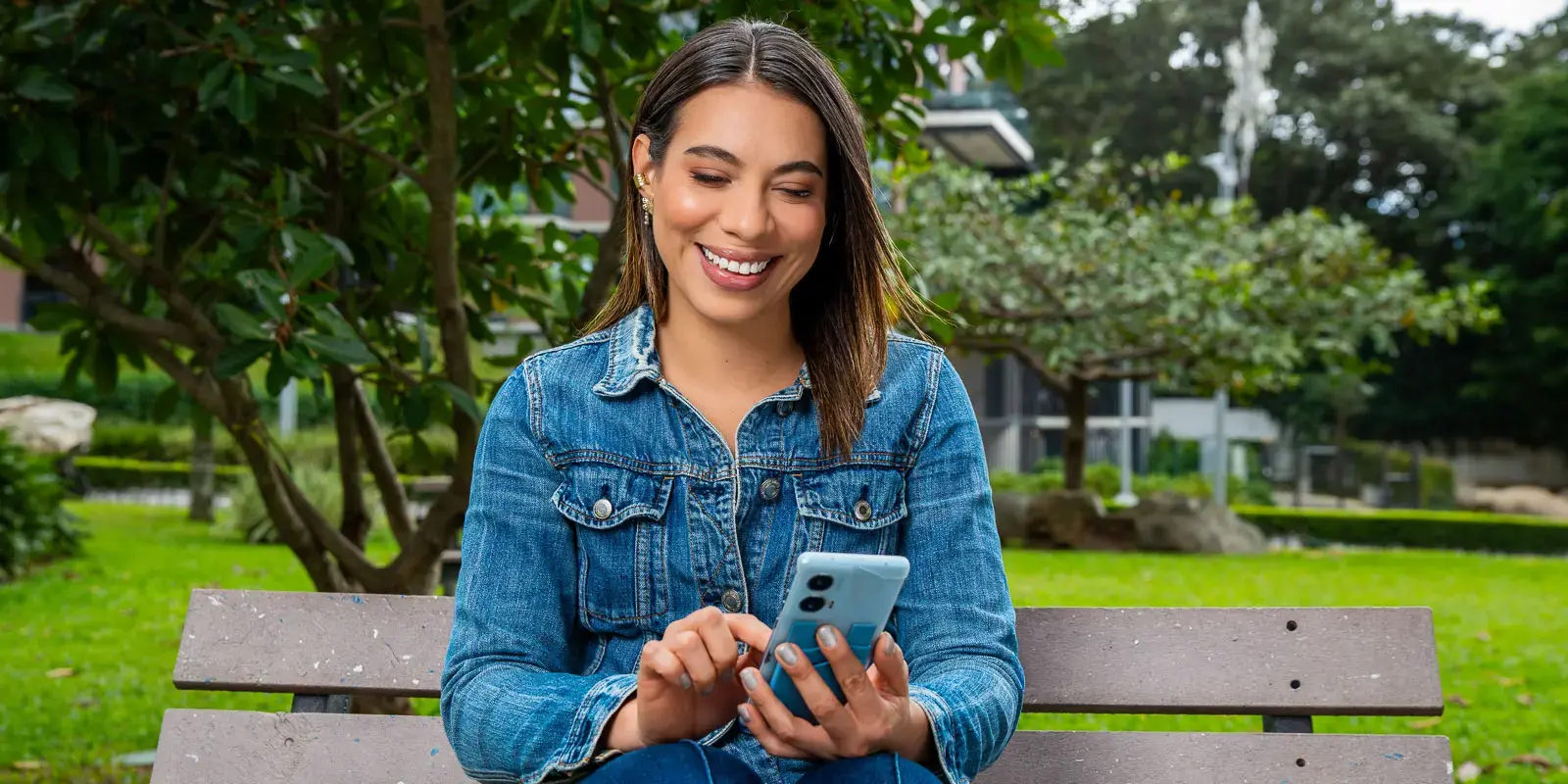 Mujer sentada en una banca al aire libre usando su teléfono móvil.