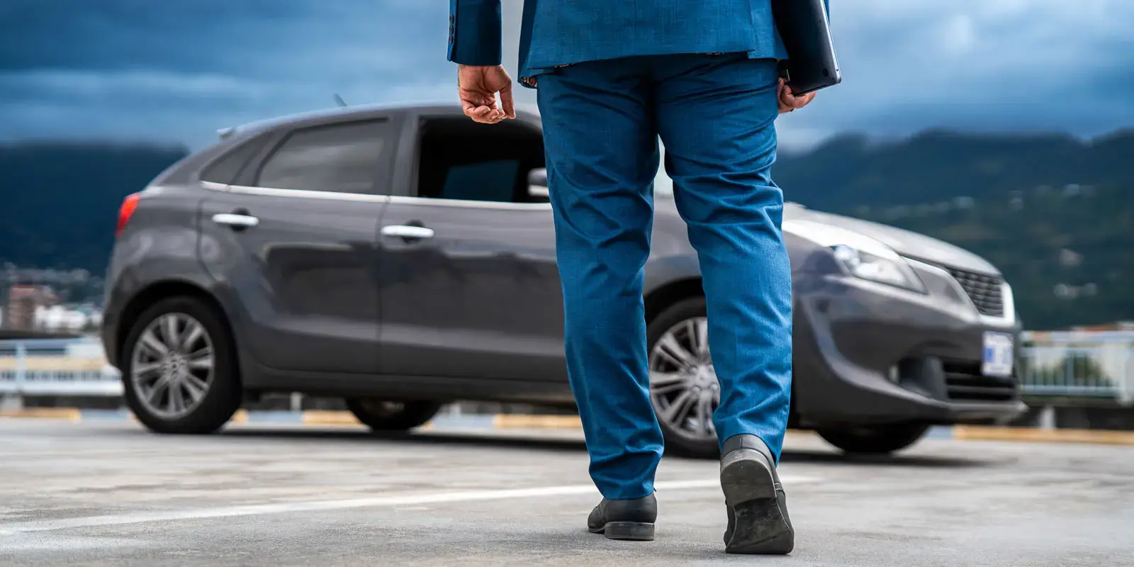Persona caminando hacia un automóvil gris en un estacionamiento exterior, vista desde atrás.