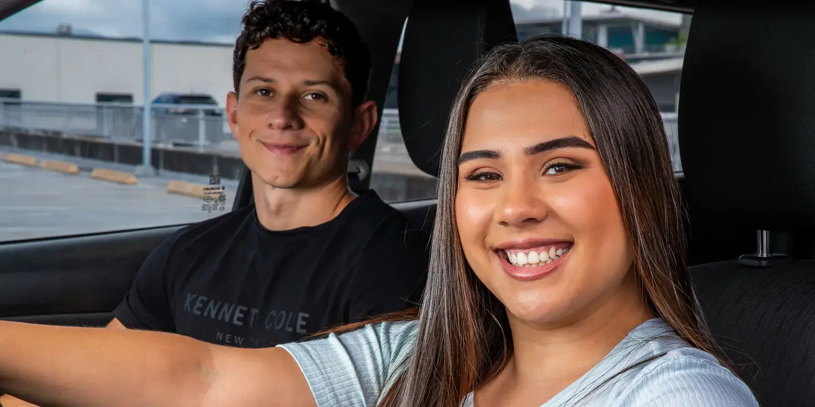 Dos personas sentadas dentro de un automóvil sonriendo hacia la cámara.