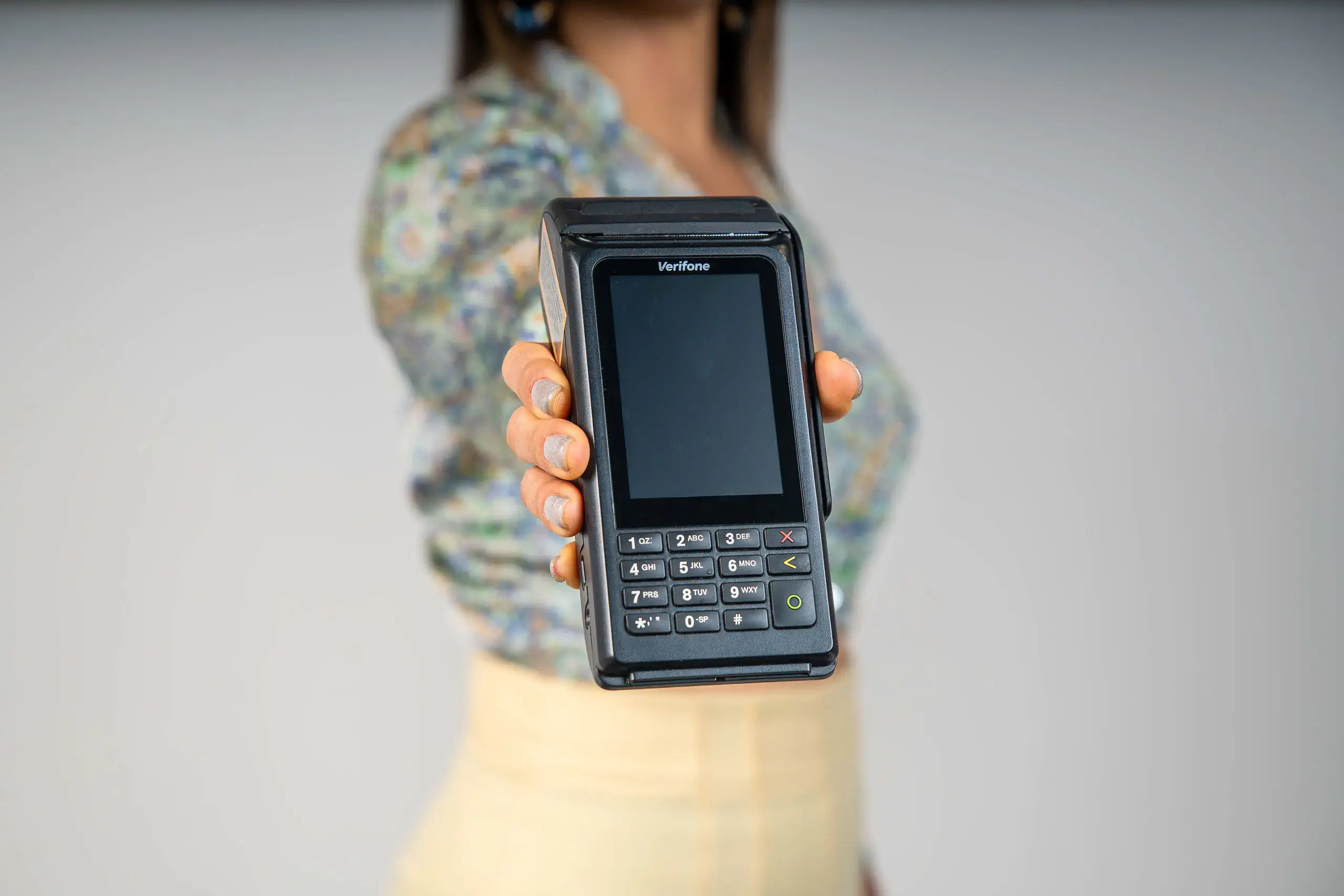 Persona sosteniendo un datáfono Verifone hacia el frente con la pantalla y el teclado visibles.