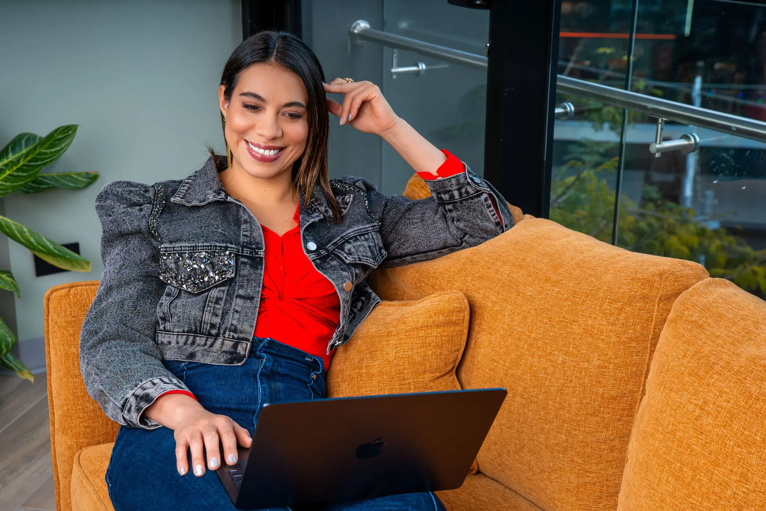 Mujer sentada en un sillón naranja usando una computadora portátil mientras sonríe.