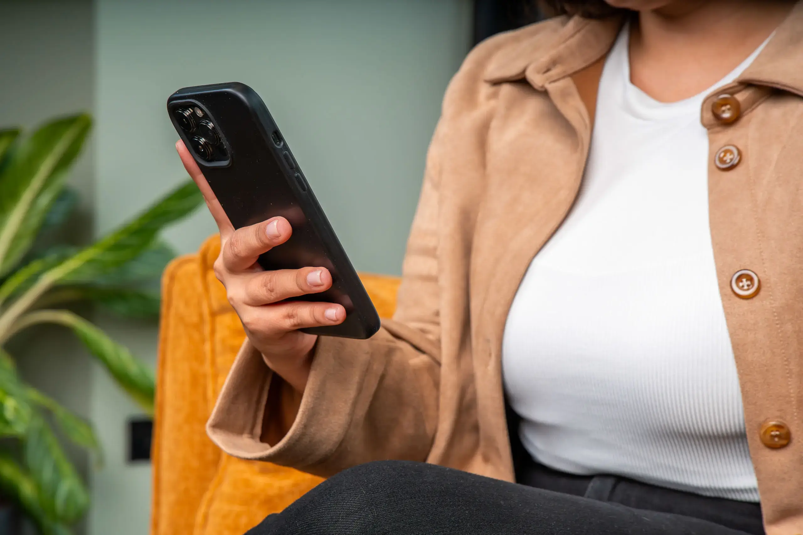 Mano de una mujer sosteniendo un teléfono móvil mientras está sentada en una silla.