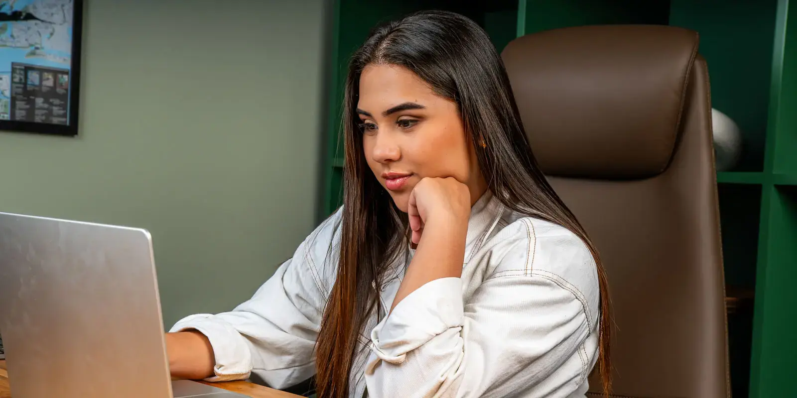 Mujer joven trabajando concentrada en una computadora portátil mientras se apoya sobre su mano.