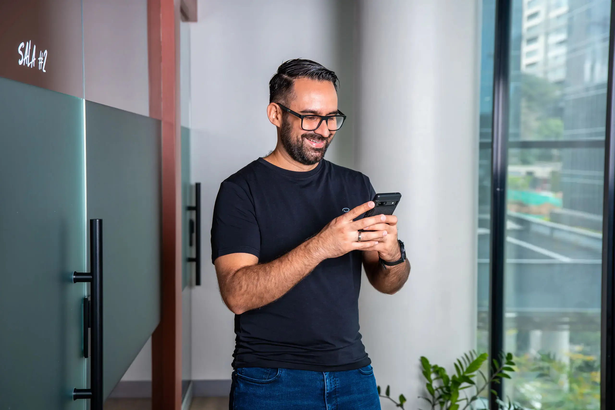 Hombre de pie usando un teléfono móvil en un pasillo con ventanales.