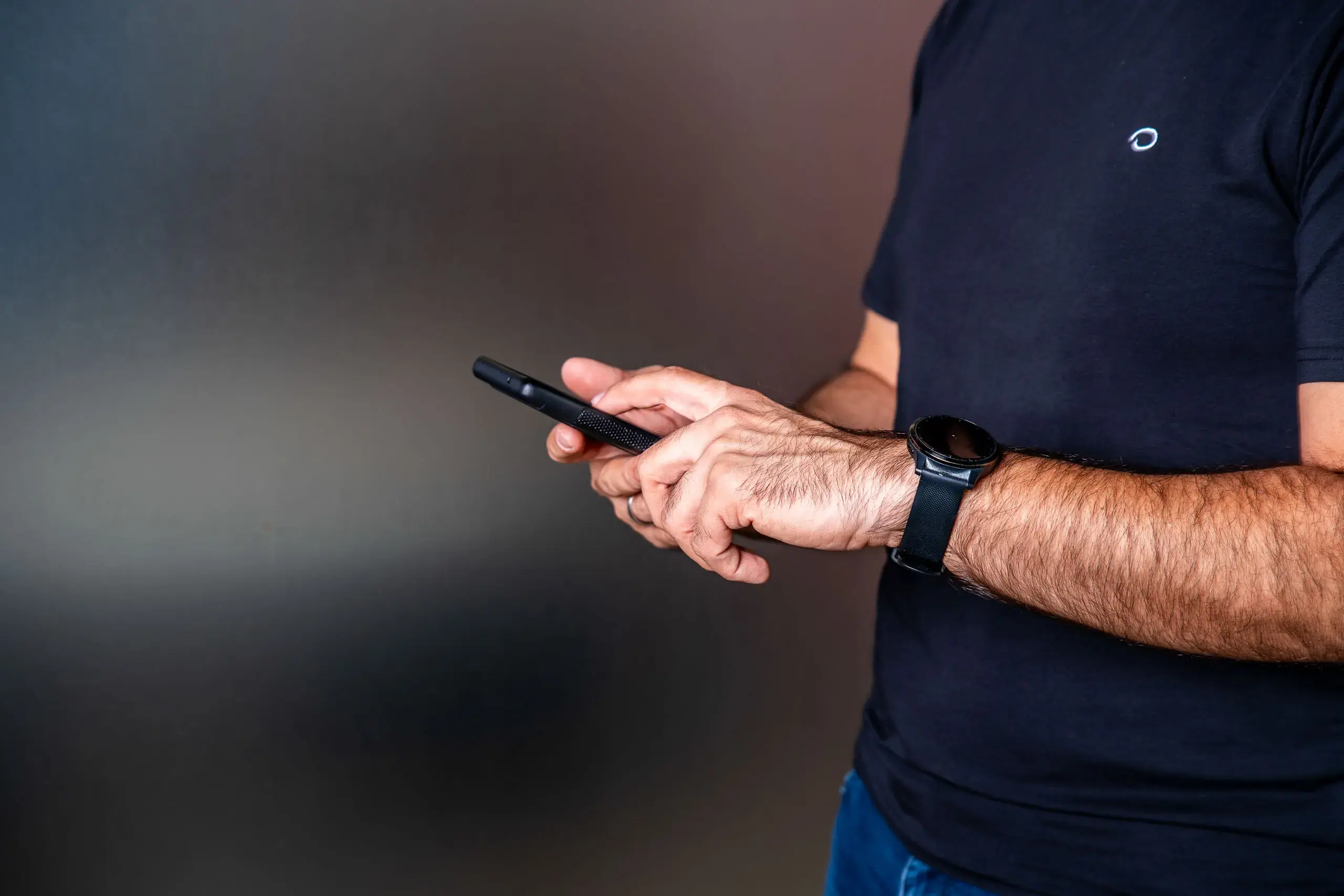 Manos de un hombre usando un teléfono móvil mientras viste una camiseta negra.