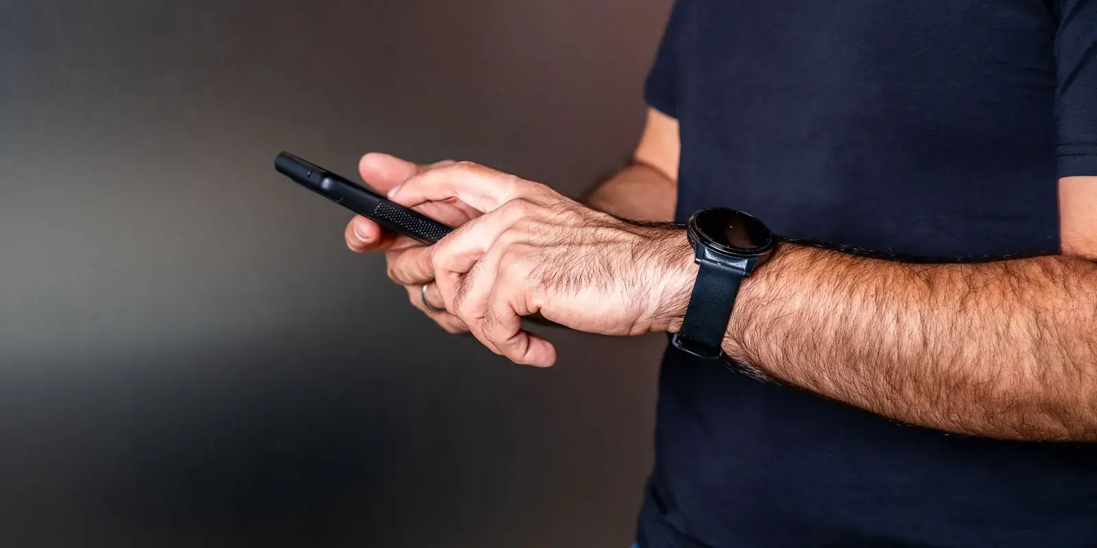 Hombre usando un teléfono móvil con ambas manos, enfocado en sus brazos y dispositivo.