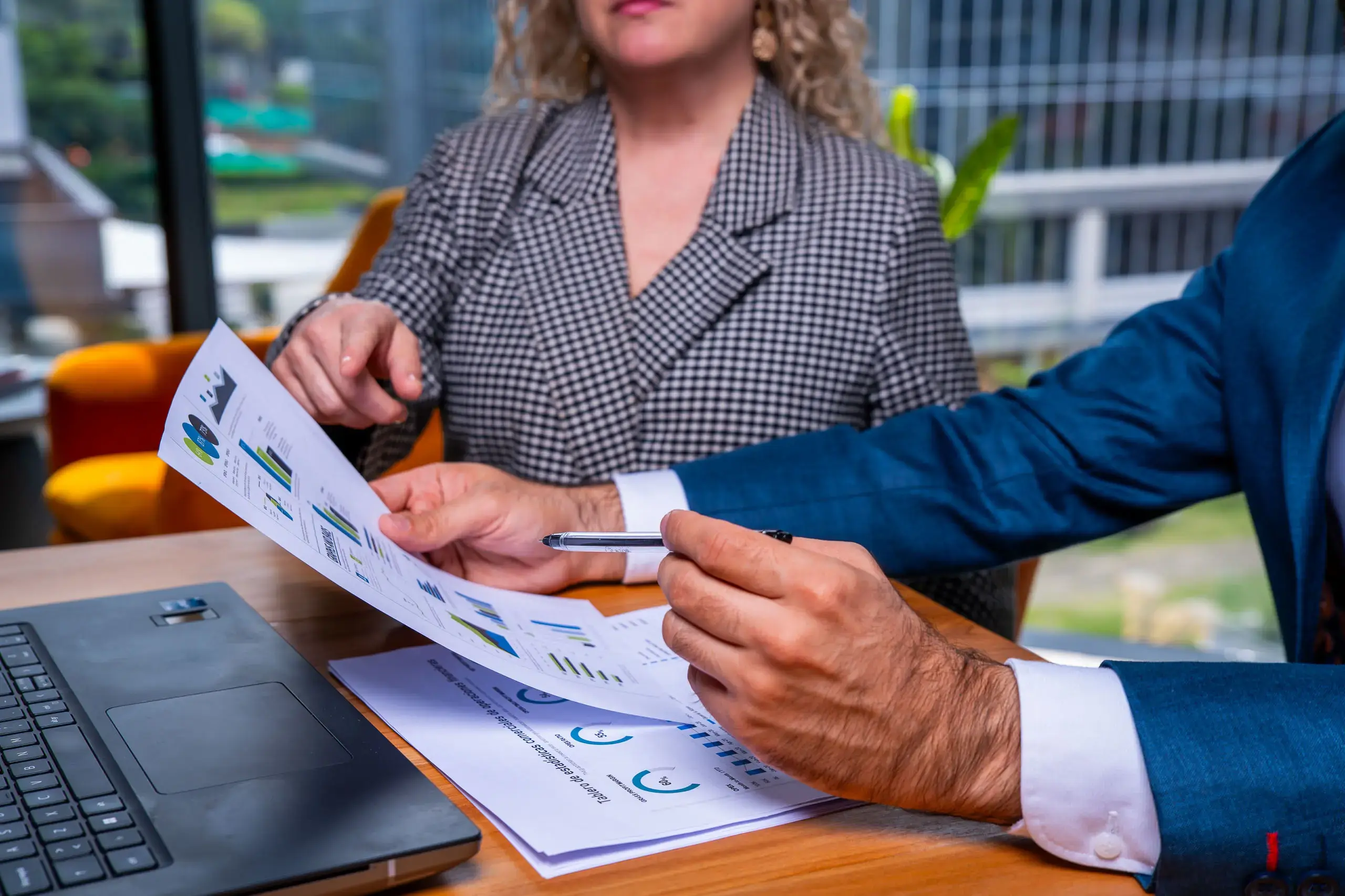 Personas revisando gráficos impresos en una mesa junto a una computadora portátil.