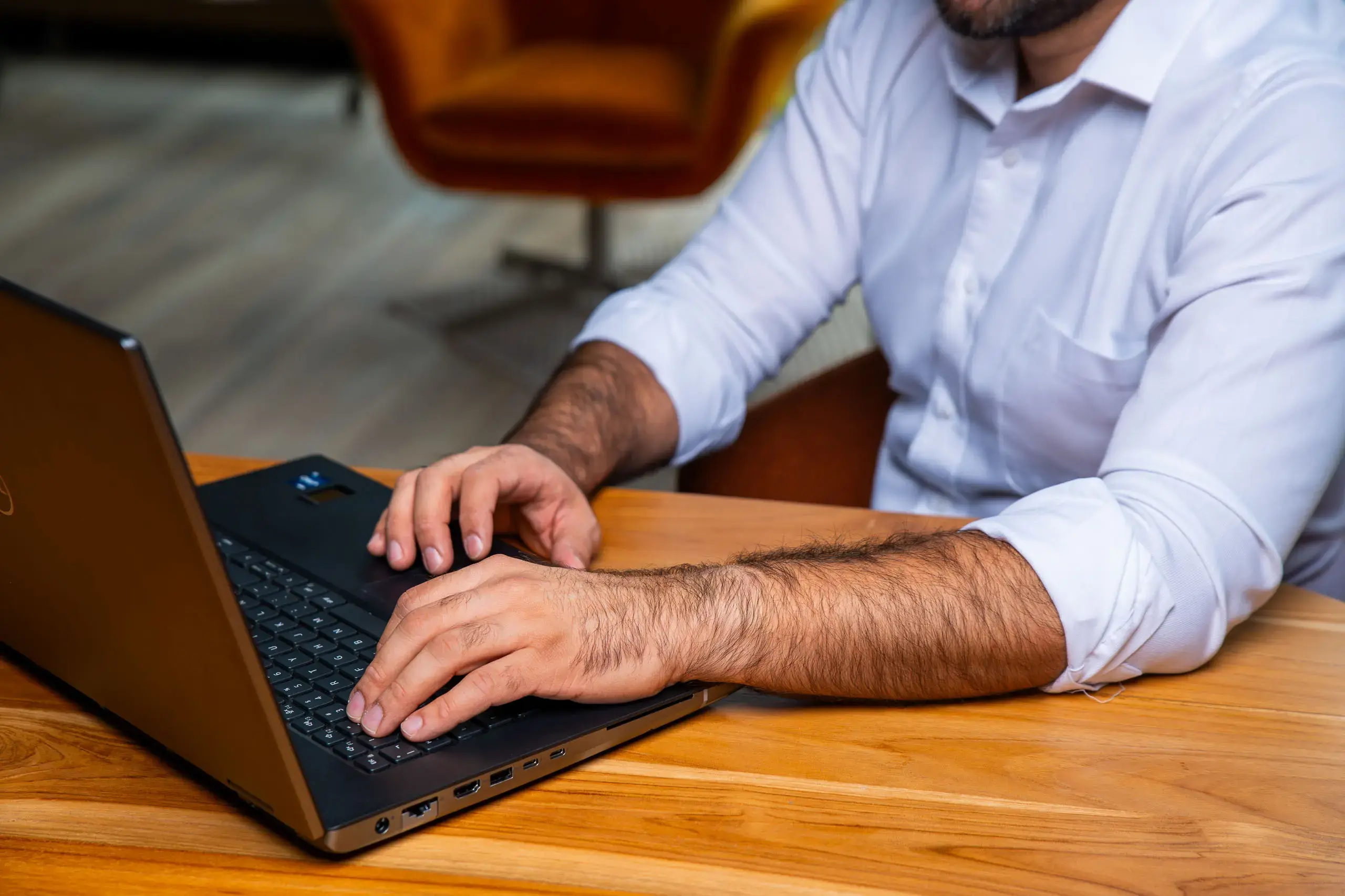 Manos de un hombre escribiendo en una computadora portátil sobre una mesa de madera.