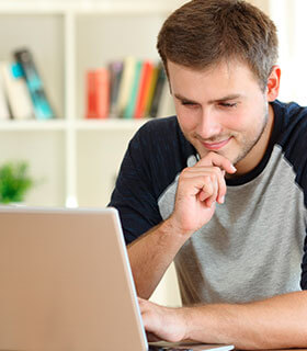 Hombre joven concentrado revisando información en su computadora portátil, en un entorno de estudio o trabajo en casa.