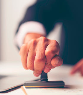 Persona aplicando un sello sobre un documento oficial sobre un escritorio, en un entorno de oficina.