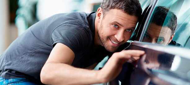 Hombre inspeccionando con detalle la carrocería de un automóvil con una sonrisa.