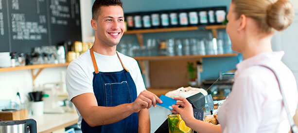 Cajero de cafetería entregando una tarjeta de pago a una clienta sonriente.