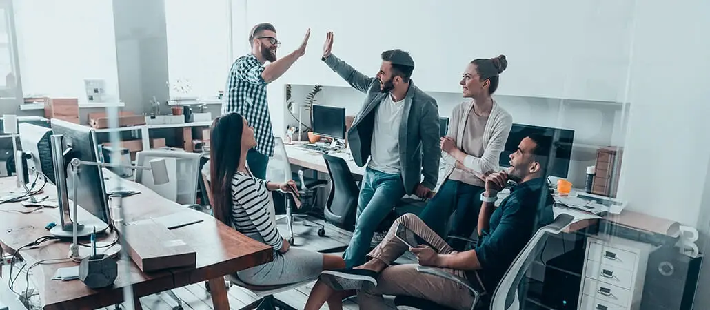 Equipo de trabajo celebrando con un choque de manos en una oficina moderna.