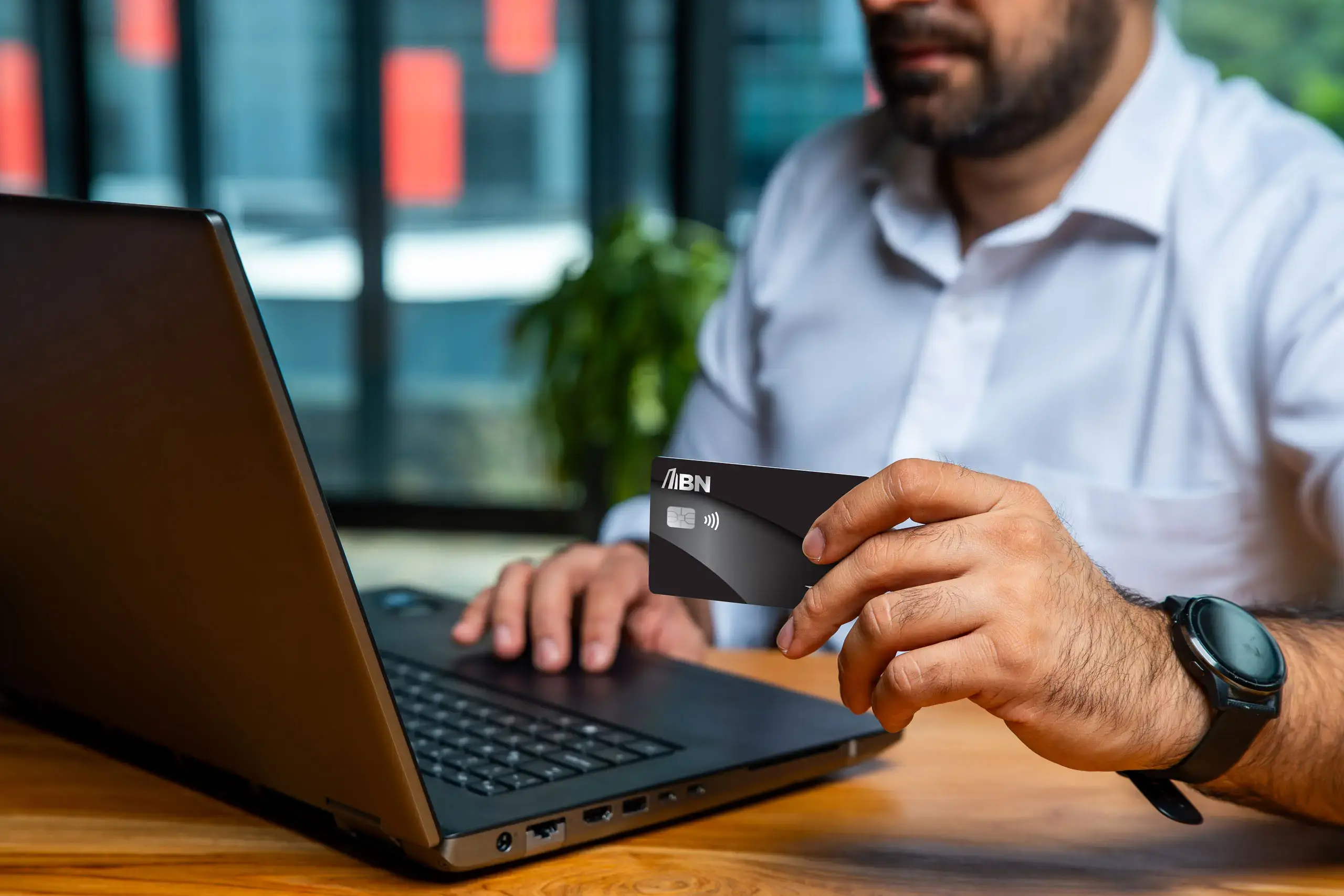 Hombre usando una computadora portátil mientras sostiene una tarjeta BN frente a la pantalla.