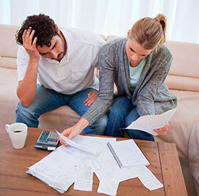 Pareja preocupada revisando facturas y cuentas sobre la mesa de su sala.
