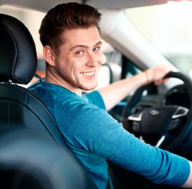 Hombre joven conduciendo un automóvil mientras sonríe y mira hacia atrás.