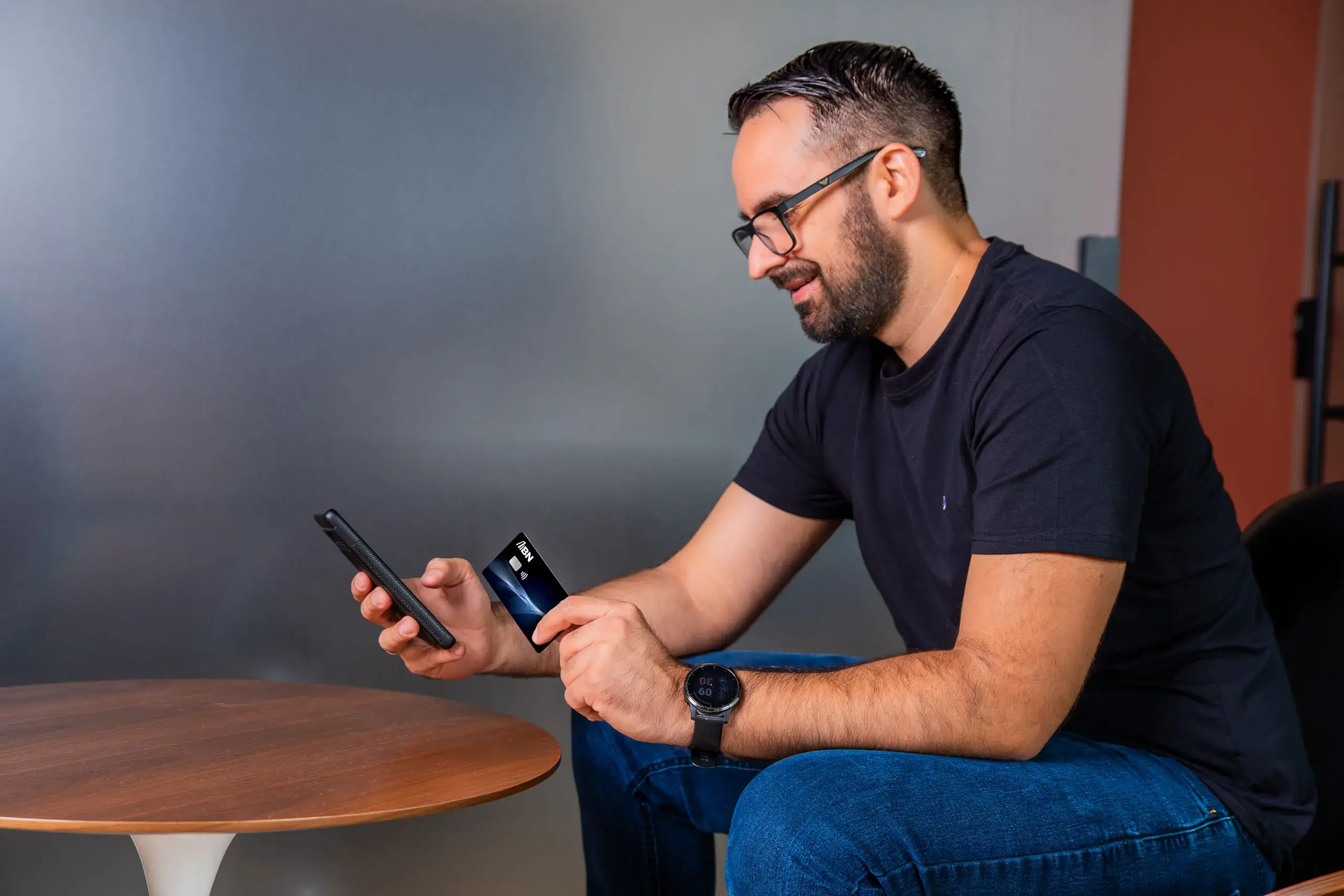 Hombre sentado usando su teléfono móvil mientras sostiene una tarjeta BN Pymes.