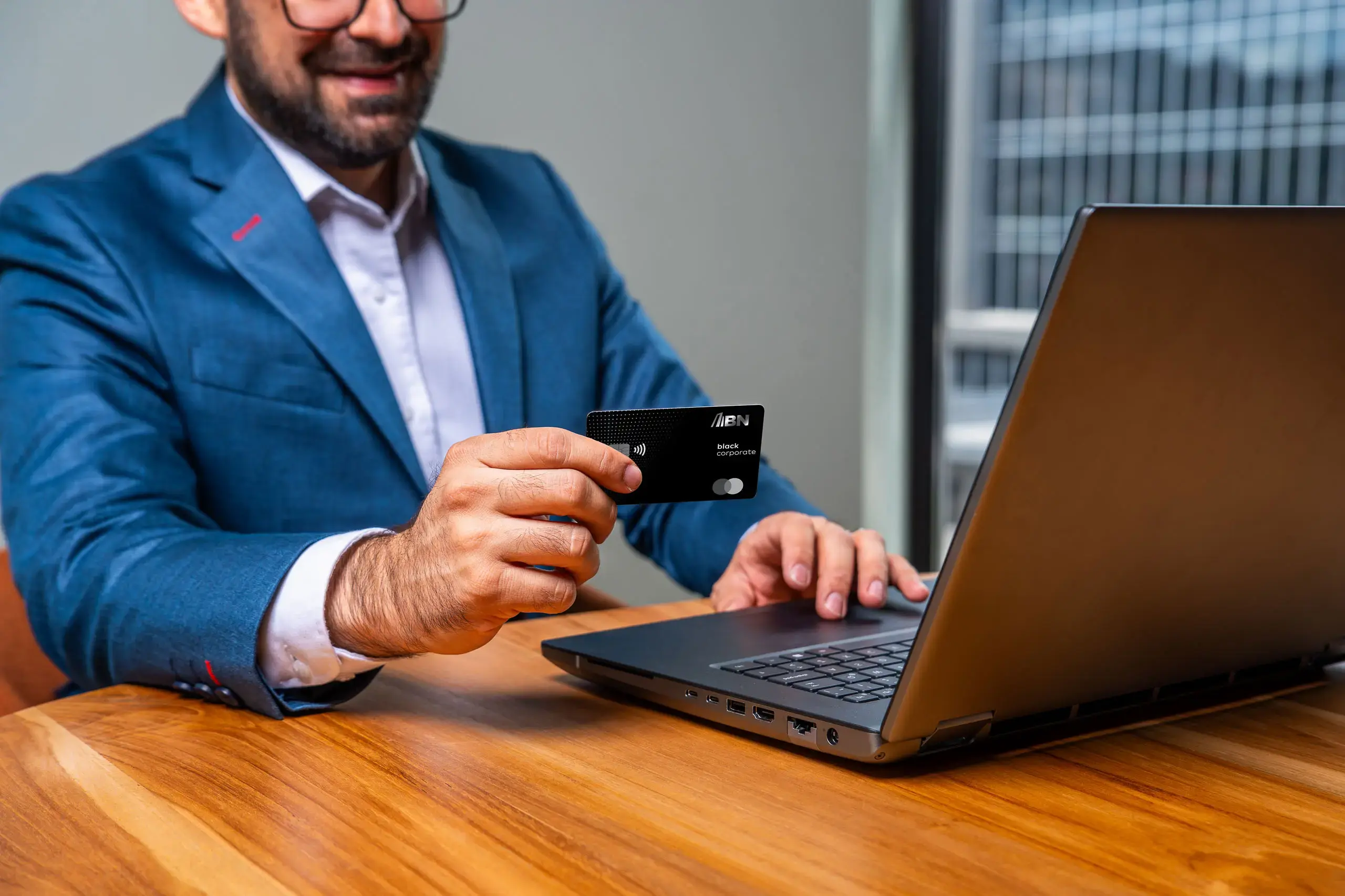 Hombre usando una computadora portátil mientras sostiene una tarjeta BN Black Corporate.