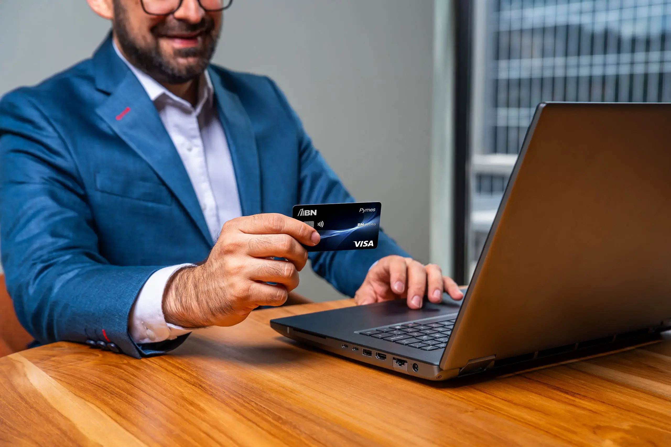 Hombre usando una computadora portátil mientras sostiene una tarjeta BN Pymes Visa.