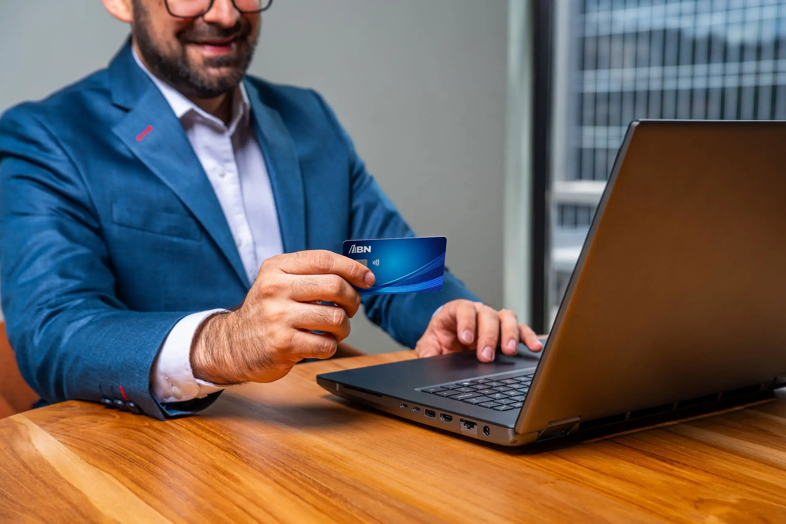 Hombre usando una computadora portátil mientras sostiene una tarjeta BN Empresarial.