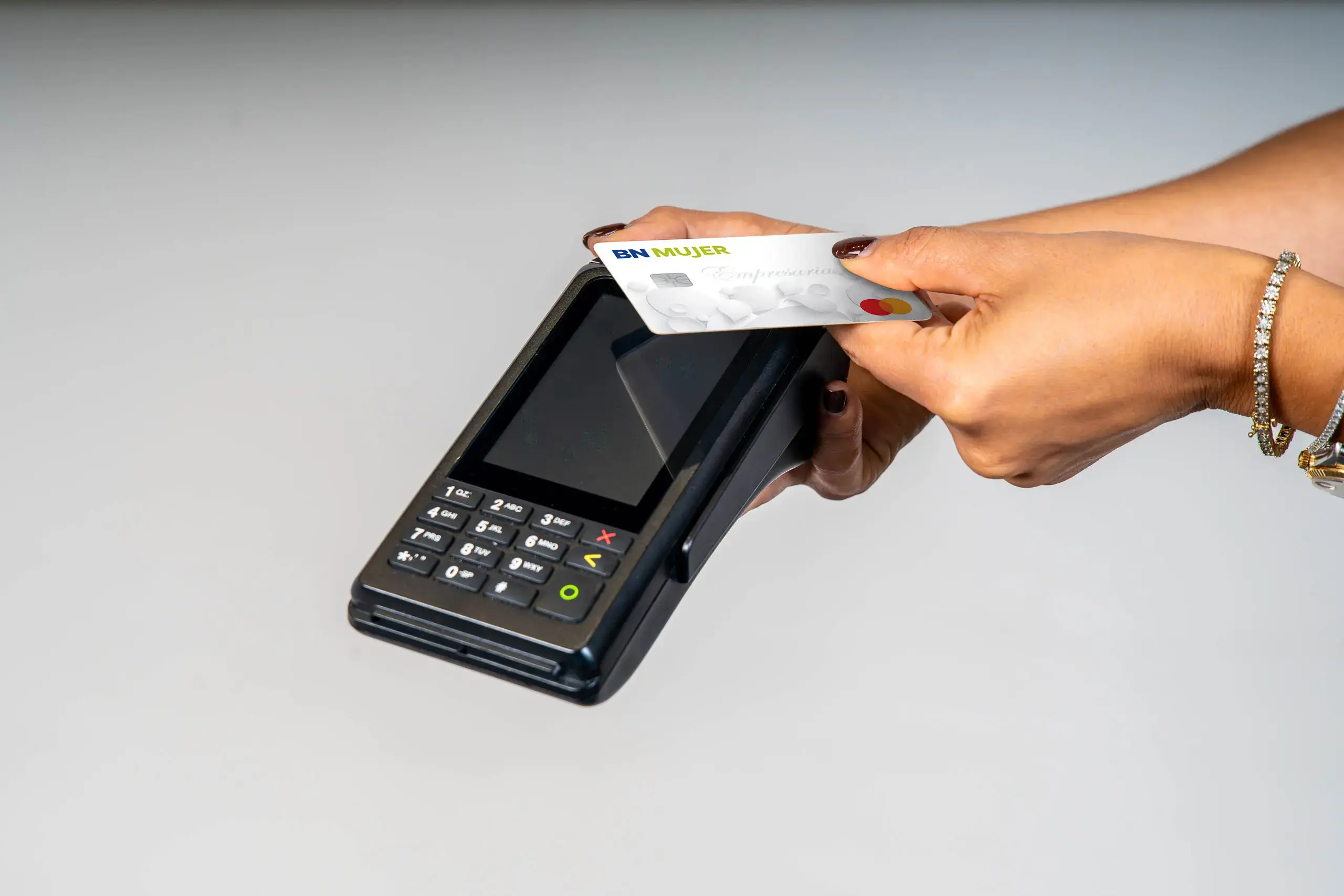 Manos acercando una tarjeta BN Mujer a un datáfono para realizar un pago.
