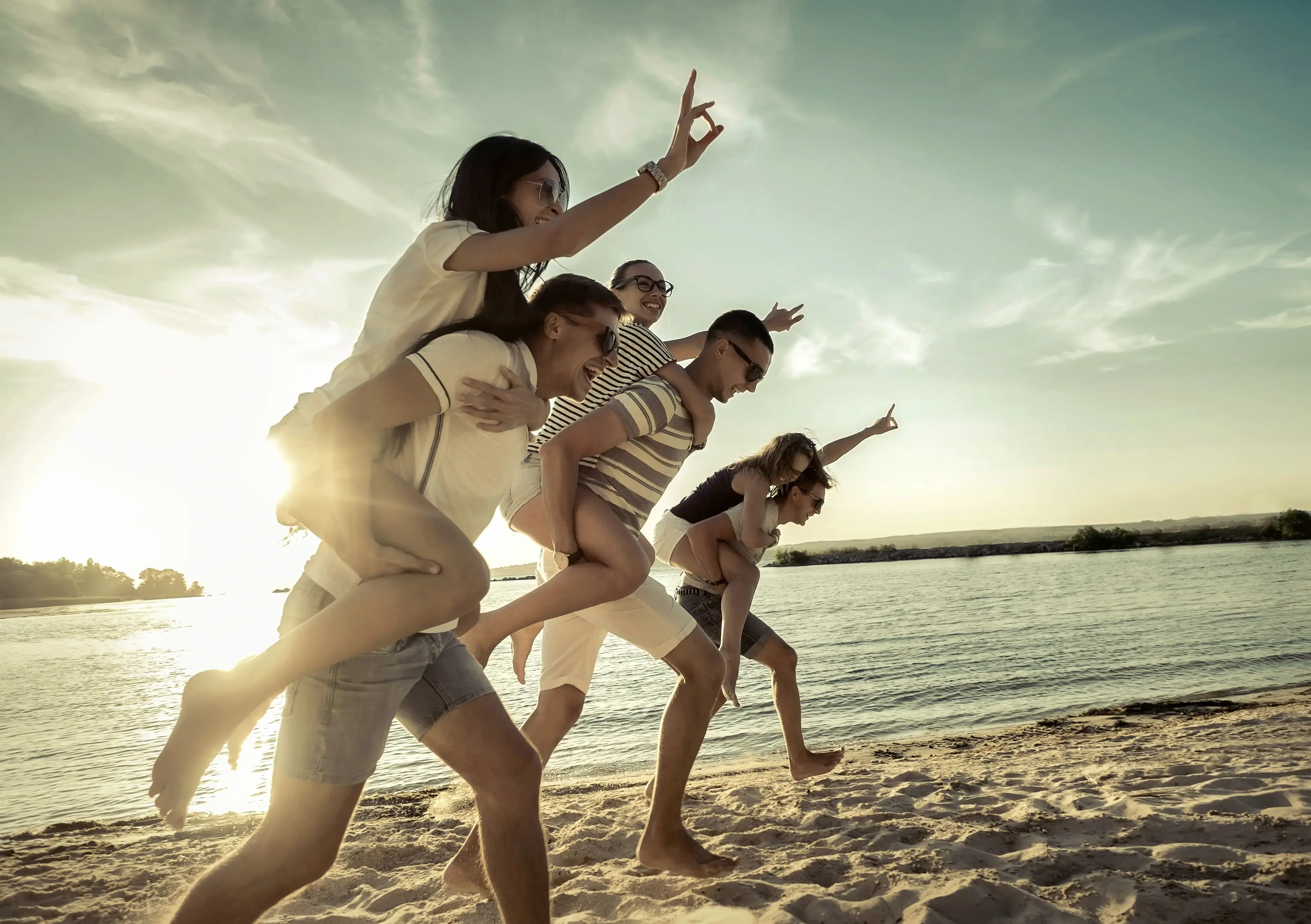 Grupo de adultos jugando y corriendo en la playa cargando a sus acompañantes al atardecer.