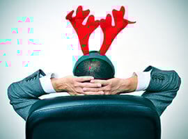 Hombre con diadema de reno descansando en una silla de oficina con las manos detrás de la cabeza.