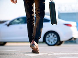 Hombre caminando hacia un auto blanco, llevando un maletín, simbolizando movilidad empresarial o ejecutiva.