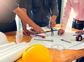 Grupo de ingenieros o arquitectos revisando planos y materiales de construcción sobre una mesa de trabajo.