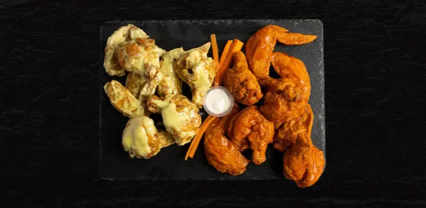 Alitas de pollo con salsas de queso y búfalo servidas con aderezo y bastones de zanahoria sobre pizarra negra